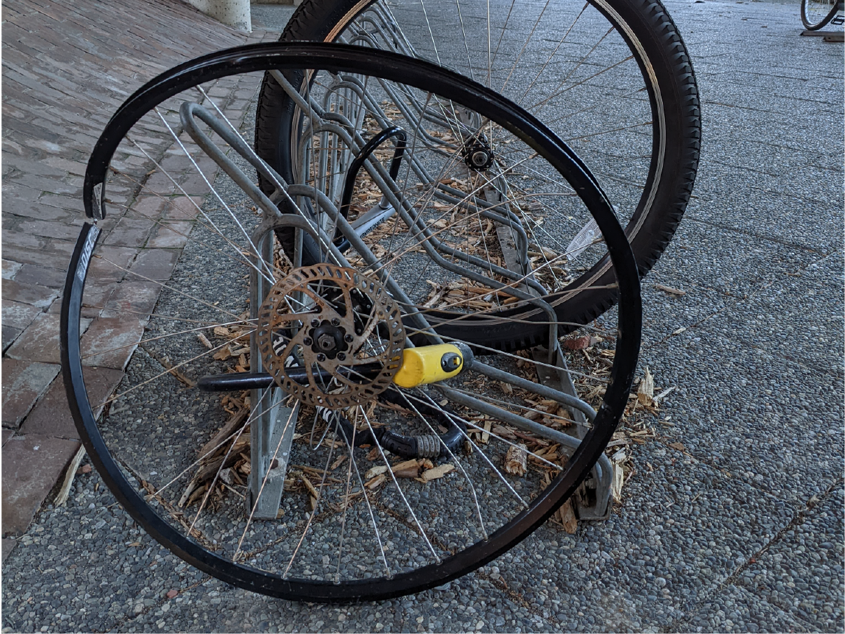 A bent higher-end wheel is locked to a bike rack with a yellow Kryptonite lock.