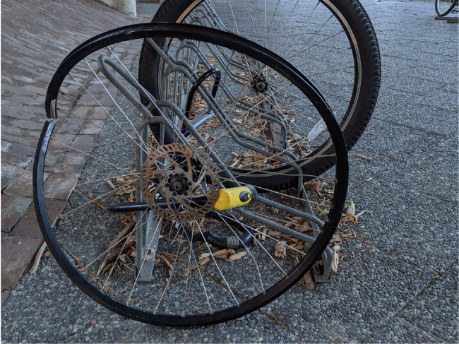 A bent higher-end wheel is locked to a bike rack with a yellow Kryptonite lock.