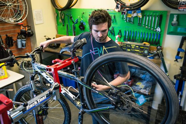 A student works on a bike held on a stand, with various tools visible in the background.
