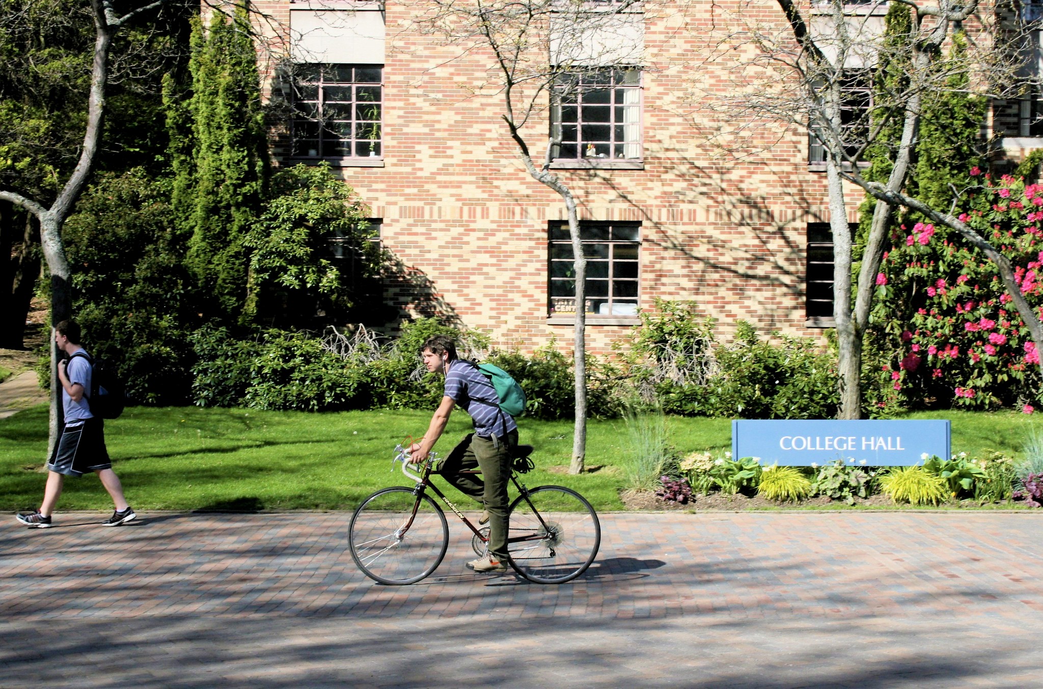 A student rides his bike past College Hall on a sunny day